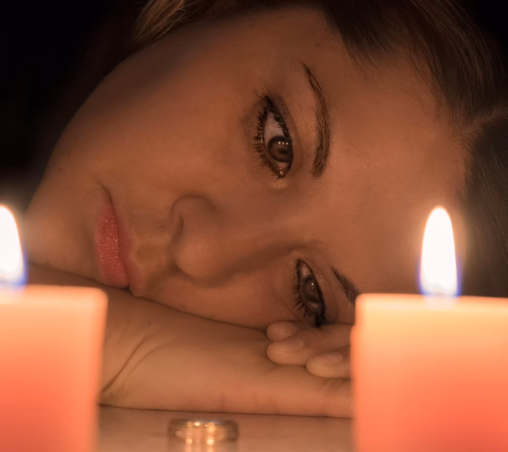 En ledsen kvinna som stirrar blint på sin vigselring med två tända ljus som skapar en dramatisk effekt.